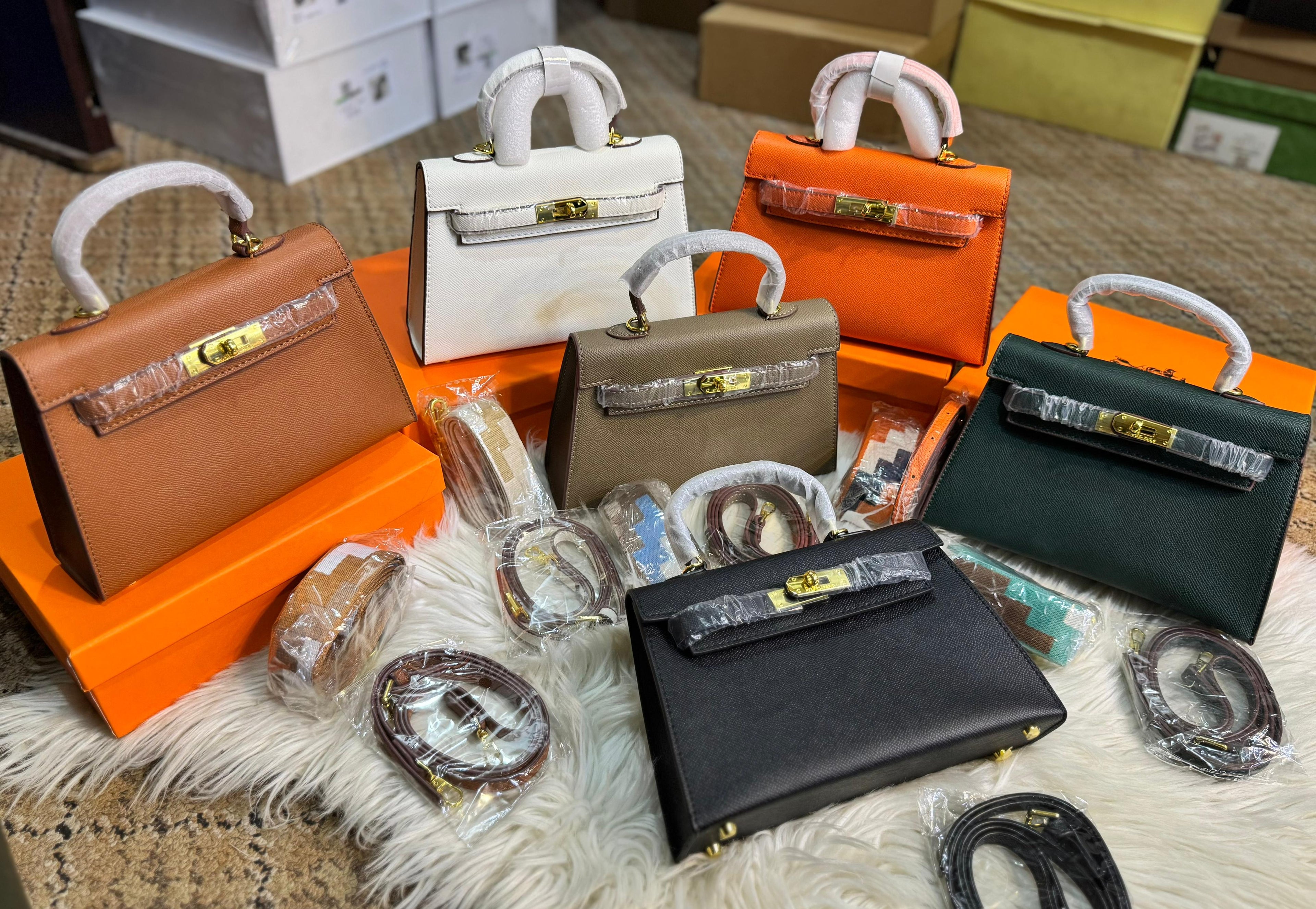 Collection of handbags in various colors with their boxes on a textured surface.